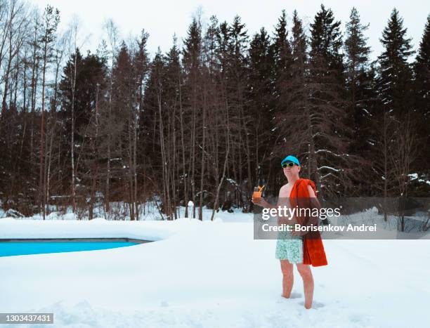 a caucasian man in sunglasses, stands near an outdoor pool, holds a drink with a straw in his hand. winter vacation at home. - swimwear stock pictures, royalty-free photos & images