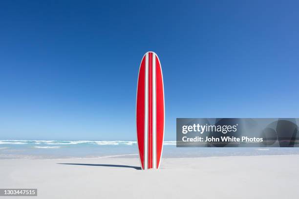 red and white striped retro surfboard with the ocean in the background. - retro beach stock pictures, royalty-free photos & images