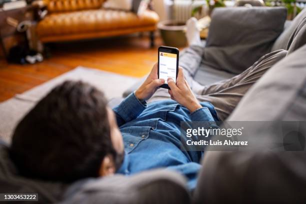 man chatting with friend on messaging app - sofa stock pictures, royalty-free photos & images