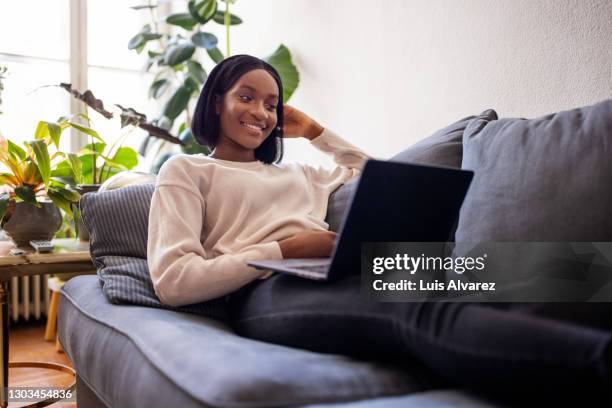 happy african woman relaxing on sofa using laptop - sitting at a laptop with facebook stock pictures, royalty-free photos & images