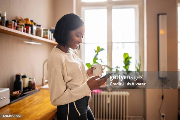 woman having coffee and texting on her phone at home - women happy photos et images de collection