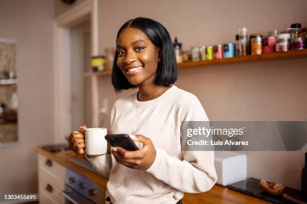 woman in kitchen with mobile and having coffee - breakfast lifestyle female stock-fotos und bilder