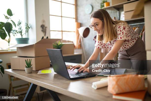 young female entrepreneur receiving new orders in her e-commerce clothing shop - parcel laptop stock pictures, royalty-free photos & images
