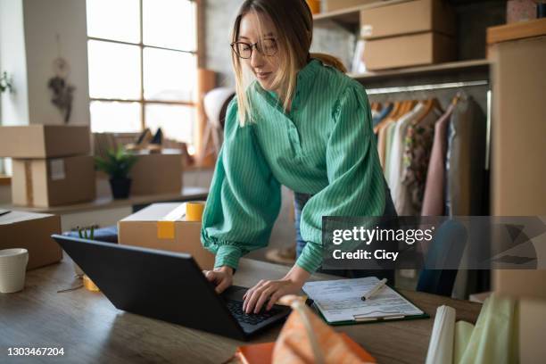 jeune femme acceptant de nouvelles commandes dans son magasin de mode d’e-commerce - industrie de la mode photos et images de collection