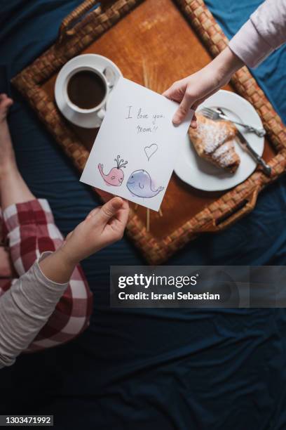 top view of a mother receiving a beautiful handmade mother's day card from her daughter along with a tasty breakfast in bed. she is on a blue colored sheet. - mother's day breakfast stock pictures, royalty-free photos & images