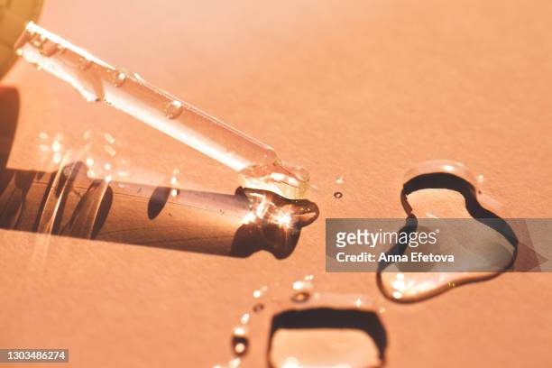 close-up of glass pipette with air bubbles spilling drops of transparent moisturizing lotion on beige background, . trendy products of the year - shiny skin stock pictures, royalty-free photos & images
