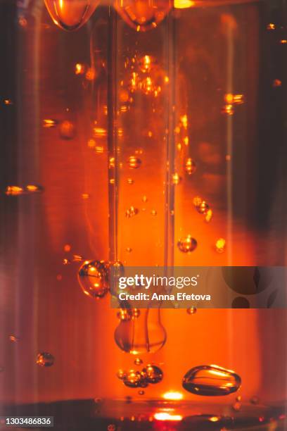 close-up pipette taking orange essential oil from transparent glass vial with air bubbles during spa procedure. trendy products of the year - bernstein stock-fotos und bilder