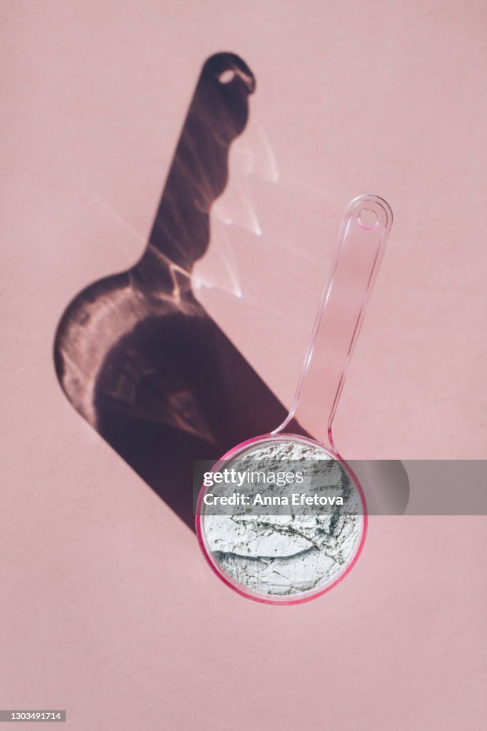 Measuring spoon with collagen powder or alginate mask on pink background