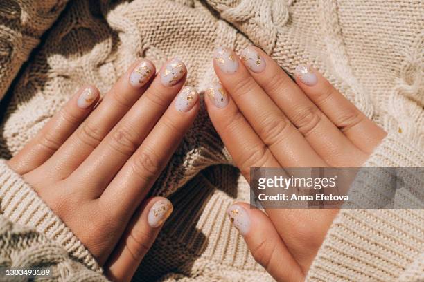 glowing hands in sweater with knitted sleeves and with nude color manicure with gold particles on knitted background. trendy colors of the year - nagelkunst stockfoto's en -beelden