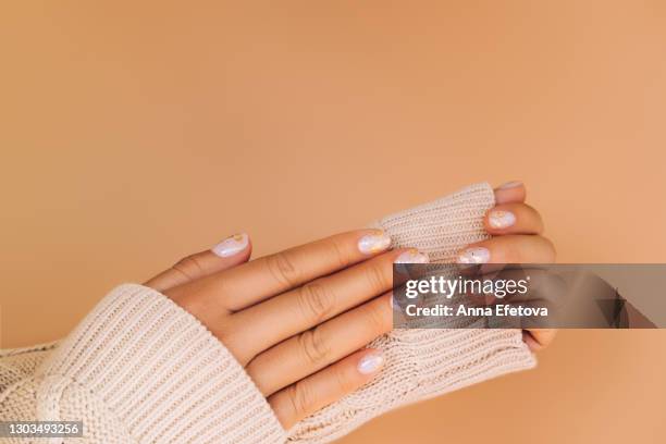glowing hands in sweater with knitted sleeves and with nude color manicure with gold particles on orange background. trendy colors of the year - manicura de diseño fotografías e imágenes de stock
