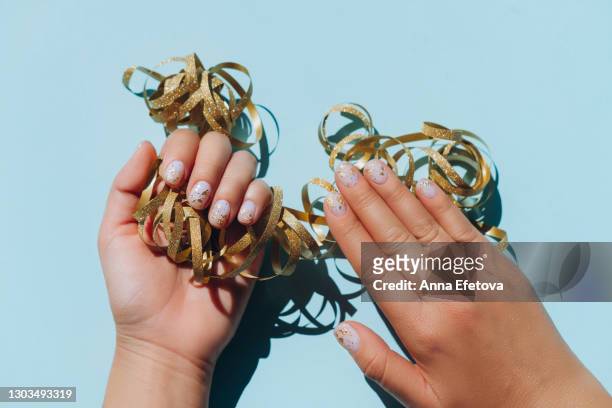 glowing hands with nude color manicure with gold particles on blue table with gold confetti. trendy colors of the year - confetti light blue background stock pictures, royalty-free photos & images