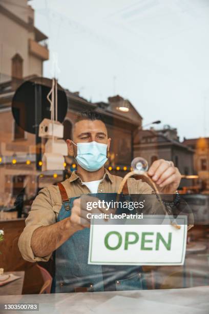 waiter of a restaurant attaching the open sign on the window - reopening banner stock pictures, royalty-free photos & images