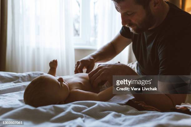 middle age caucasian father changing diaper for newborn baby daughter. male man parent taking care of child at home alone. authentic lifestyle candid moment. single dad family life concept. - changing nappy stock pictures, royalty-free photos & images