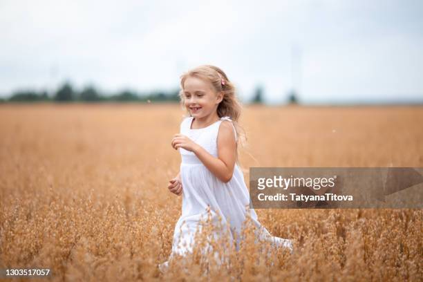 cute little girl with long blond hair in white dress happy in the oat field - latvia girls stock pictures, royalty-free photos & images