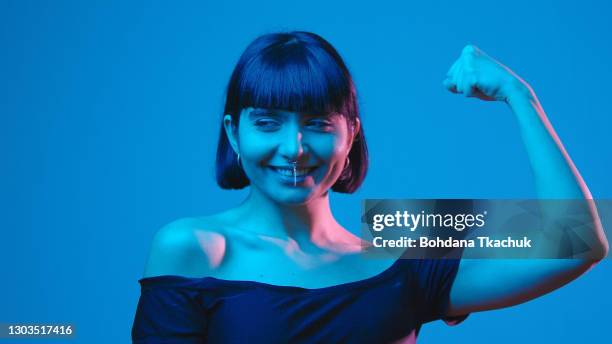 young woman flex biceps isolated on blue neon copyspace - perfect female body shape stock pictures, royalty-free photos & images