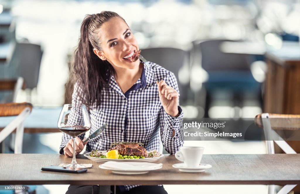 Woman enjoys a bite of medium steak on beans sitting in a restaurant.