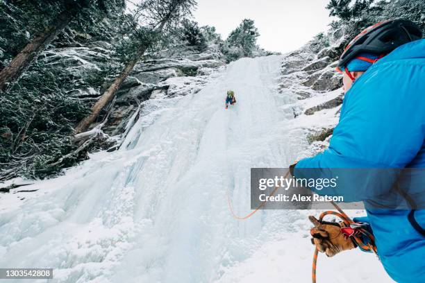 point of view photo of two ice climbers climbing with one belaying - eisklettern stock-fotos und bilder