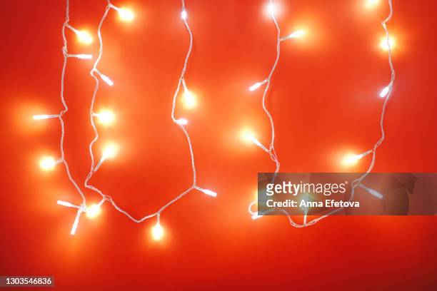 defocused bright christmas background with glowing bokeh multicolored garland lights shining in red illumination. new year celebration concept - cadena de luces fotografías e imágenes de stock