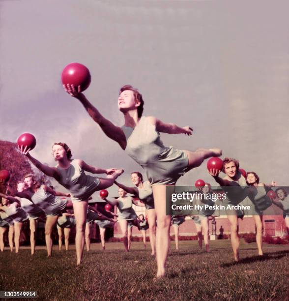 General view as women exercise and balance on one leg while holding a ball circa 1955.