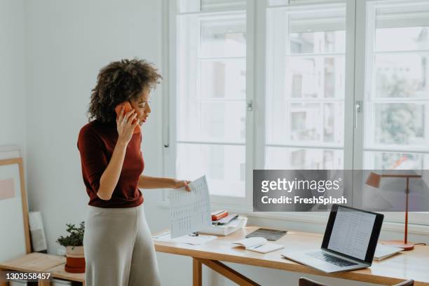 empresaria ocupada hablando por teléfono en su oficina de inicio - adaptable fotografías e imágenes de stock
