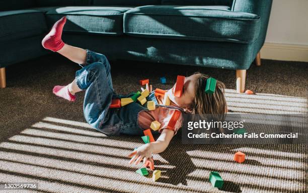 little girl playfully falls backwards as colourful wooden blocks scatter - giocare foto e immagini stock