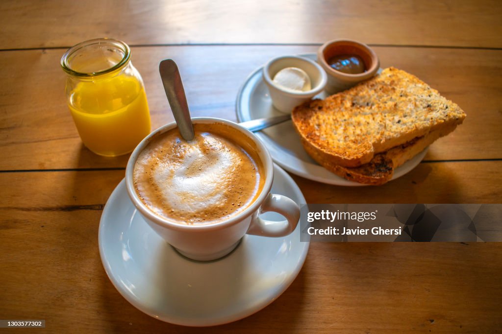 Café con leche y tostadas de campo con queso crema y mermelada, y jugo exprimido de naranja