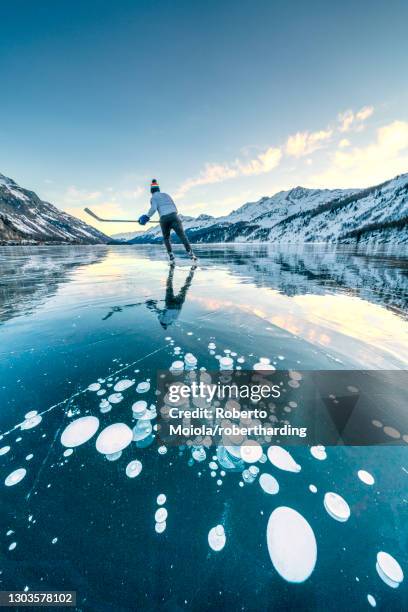 ice hockey player skating on frozen lake sils covered of bubbles, engadine, canton of graubunden, switzerland, europe - pond hockey stock pictures, royalty-free photos & images