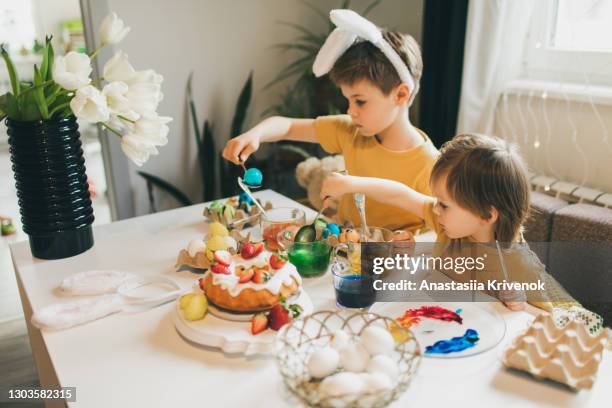 two cute smal siblings painting easter eggs at cozy home. - ausmalen stock-fotos und bilder