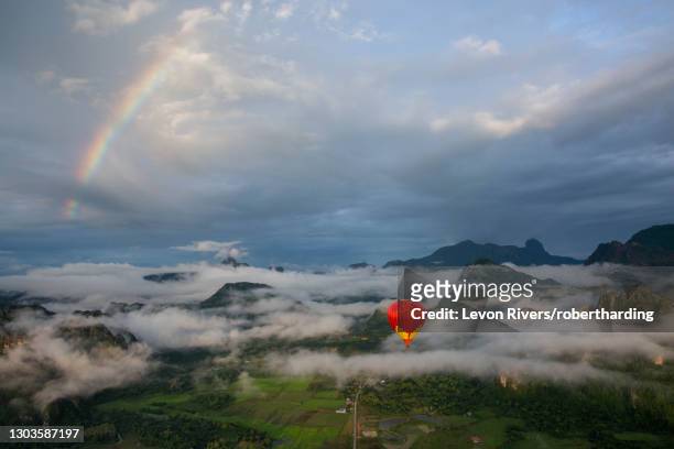 a sunrise over vang vieng, with a rainbow over the clouds, as a hot air balloon rises in the foreground, laos, indochina, southeast asia, asia - vang vieng balloon stockfoto's en -beelden