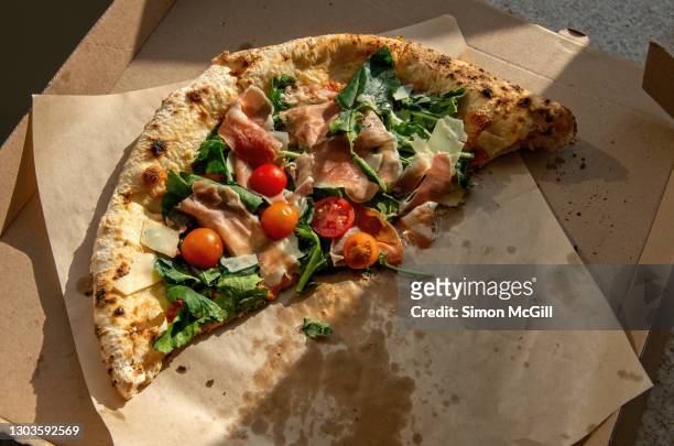 half a woodfired sourdough pizza with prosciutto/parma ham, cherry tomatoes, arugula, mozzarella and parmesan reggiano in a cardboard pizza box - leftover stock pictures, royalty-free photos & images