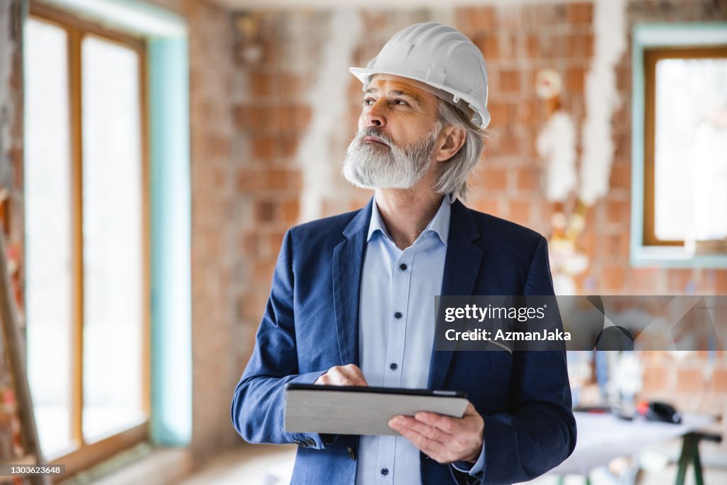 Adult male building supervisor taking notes on a tablet while inspecting the interior of a building under construction