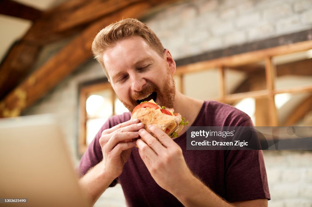Redhead man enjoying while eating sandwich in the morning at home.