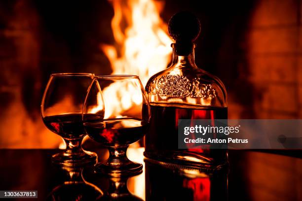two glasses of cognac and a bottle near the fireplace. cozy evenings by the fireplace - cognac glass stock-fotos und bilder