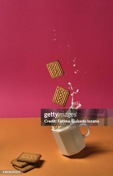 cookies falling into glass with milk, while the glass slides and spills the milk. - coffee splash stock-fotos und bilder