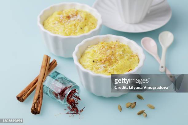 rice pudding with saffron, cinnamon, cardamom in a baking dishes and a cup of tea on blue background - rice pudding stock pictures, royalty-free photos & images