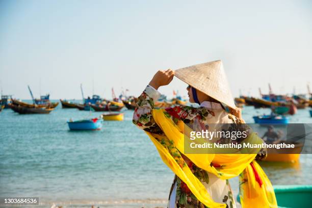 a vietnamese woman in vietnam traditional clothes with traditional boats near the shore of vietnam shows beautiful scenery of the beach. - hot vietnamese women stock pictures, royalty-free photos & images