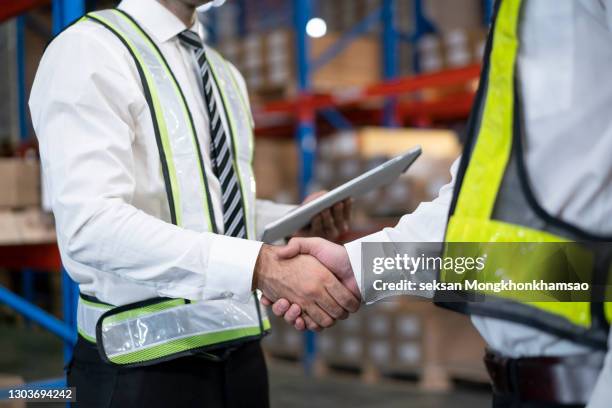 two satisfied business man standing in warehouse with helmets on their head. shaking hands and closing good job cooperation. - business hand shake with arabs stock pictures, royalty-free photos & images