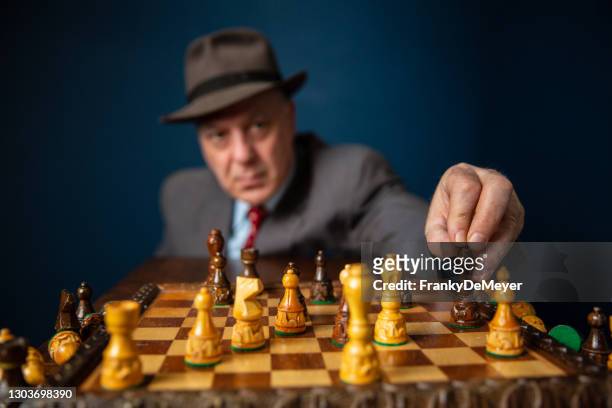 with focus on the chess pieces on the chess board, a senior mature man in retirement is playing solo chess alone as hobby, dressed in suite and hat - chess stock pictures, royalty-free photos & images