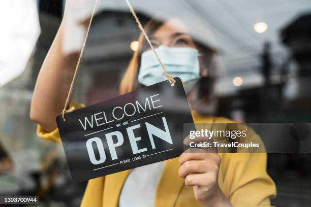 coffee shop woman owner with face mask, open after lockdown quarantine. reopening of a small business activity after the covid-19 emergency. business sign that says now we are open support local businesses hang on door at entrance. - open sign on door stock-fotos und bilder