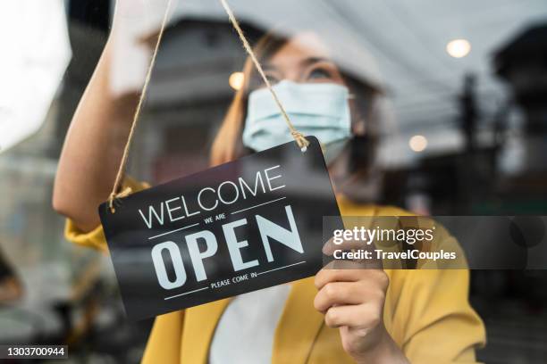 coffee shop woman owner with face mask, open after lockdown quarantine. reopening of a small business activity after the covid-19 emergency. business sign that says now we are open support local businesses hang on door at entrance. - restaurants open during lockdown stock pictures, royalty-free photos & images