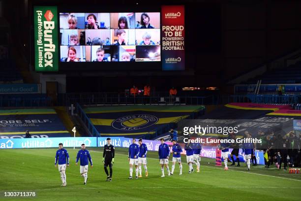 Players of Leeds United led by Liam Cooper make their way out for the start as young fans watch on from the big screen during the Premier League...