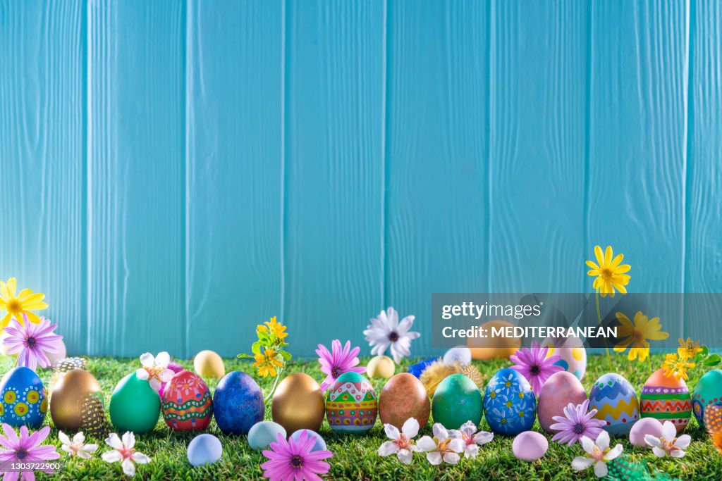 春の花と芝の草と青い木製の壁にイースターエッグ
