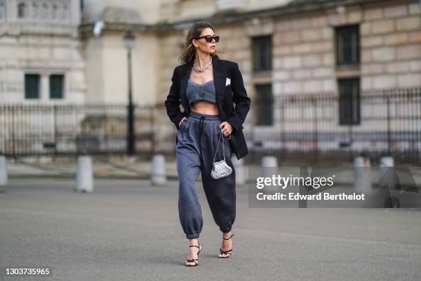 Natalia Verza wears a total Miu Miu look made of sunglasses, earrings, a chain metallic necklace, a black oversized blazer jacket, gray bras, a Miu...