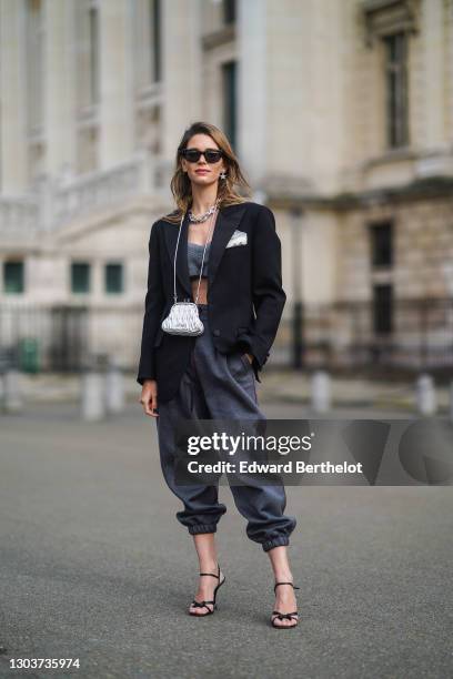 Natalia Verza wears a total Miu Miu look made of sunglasses, earrings, a chain metallic necklace, a black oversized blazer jacket, gray bras, a Miu...