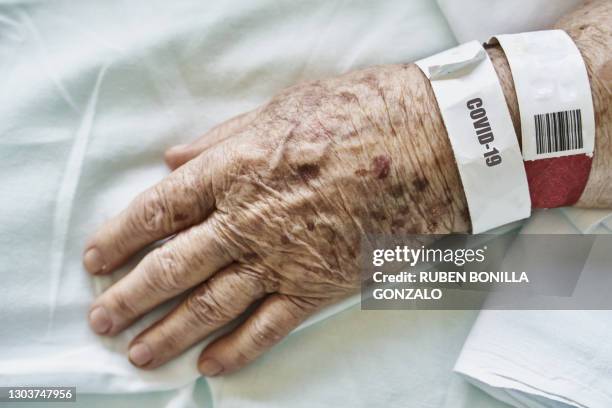 close-up hand of a senior person on hospital bed with medical bracelet with word covid-19 - hospital bracelet stock pictures, royalty-free photos & images