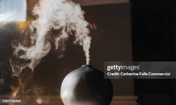 a thick mist gently rises and falls from an oil diffuser in a home environment - essential oil stock pictures, royalty-free photos & images