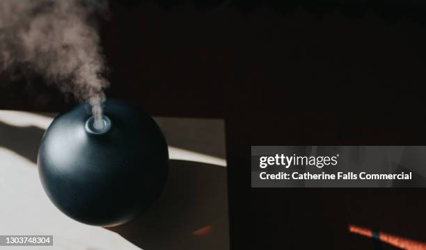 a thick mist gently rises from an oil diffuser, used in aromatherapy - humidifier stock pictures, royalty-free photos & images