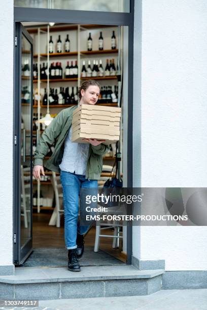 young delivery man carrying stack of pizza boxes out of the pizzeria - drinks carton - fotografias e filmes do acervo