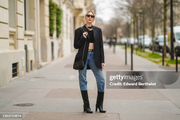 Emy Venturini wears sunglasses, golden earrings, a golden large chain necklace, a black cropped top from Elisabetta Franchi, a black oversized blazer...