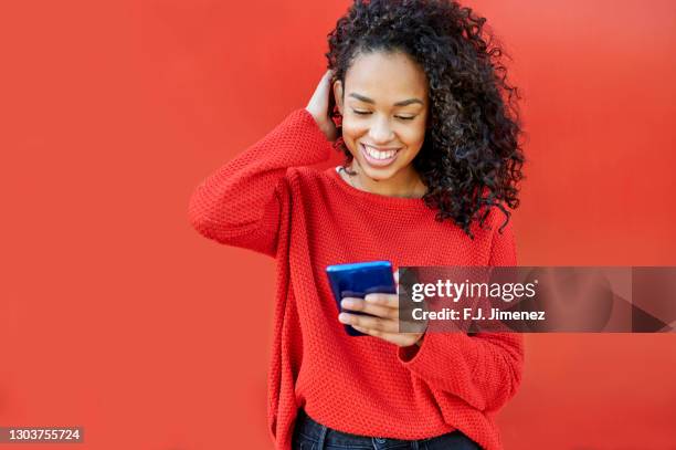 woman using mobile phone in front of red wall - before the 24 stock pictures, royalty-free photos & images